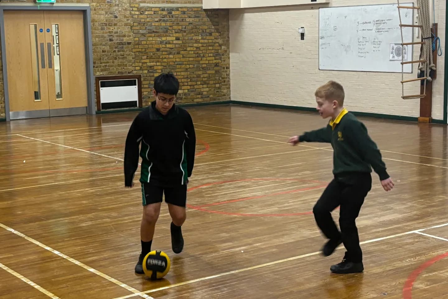 Two pupils playing football during an indoor activity session